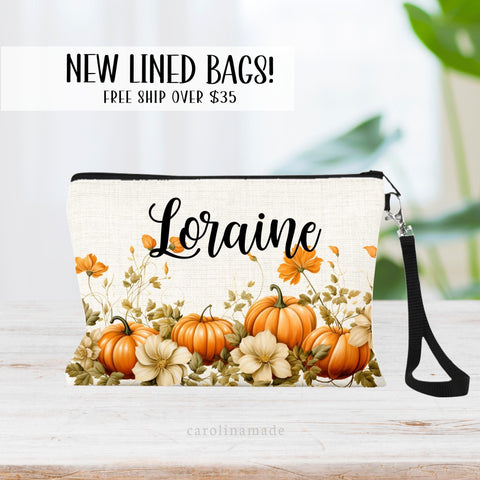 This linen wristlet features pumpkins along the bottom border of the bag with greenery and flowers. It is personalized at the top with your name.